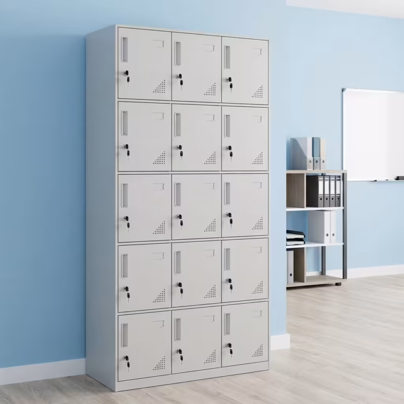 Premium 15 Locker Office Steel Cabinet in a professional light grey powder-coated steel finish, showcasing a 3x5 grid layout of fifteen closed locker doors with recessed handles, cylinder locks with keys inserted, name card frames, and stamped bottom ventilation patterns, standing flat on smooth light wood flooring against a textured grey wall.