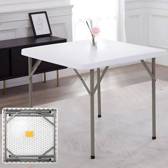 Folding Plastic Table with a square white plastic tabletop, rounded corners, slim grey metallic-toned legs, pivoting locking braces, and black protective feet caps.