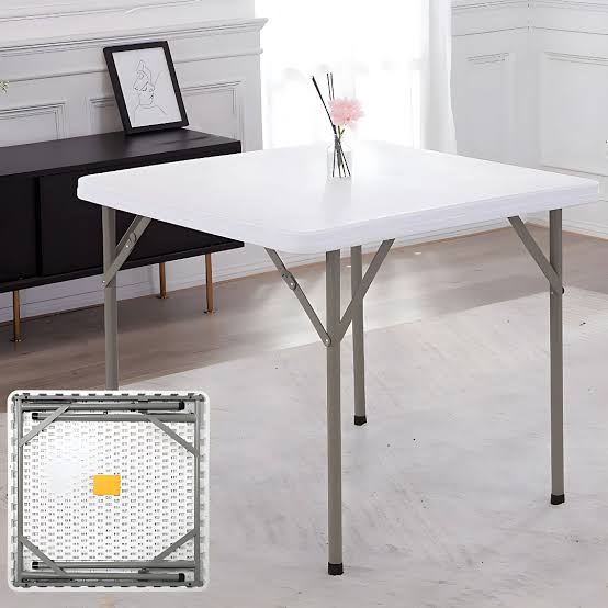 Folding Plastic Table with a square white plastic tabletop, rounded corners, slim grey metallic-toned legs, pivoting locking braces, and black protective feet caps.