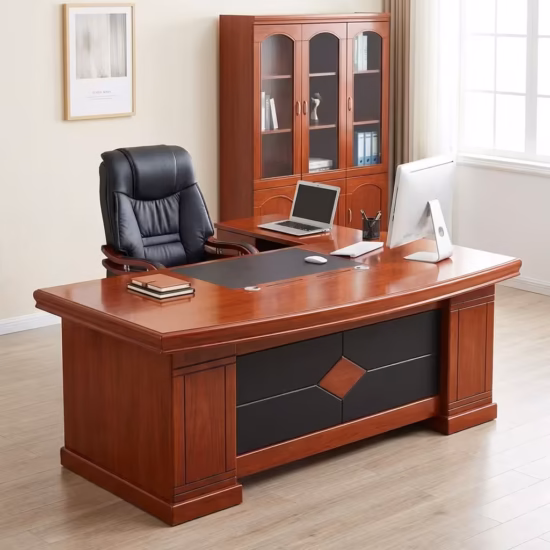 Premium L-Shaped Desk With Side Return in a rich mahogany finish, featuring an integrated black leather center desk blotter mat, a front modesty panel with a diamond-embossed black faux leather center design, and an attached side return console supporting an open laptop, paired with a high-back black mesh office chair on a polished wood floor.
