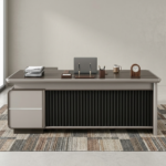 Premium CEO Modern Executive Office Table in a dark charcoal-brown woodgrain finish, featuring a vertical black fluted slatted front modesty panel, an integrated cream-colored side storage drawer pedestal, and a built-in black leather desk blotter mat supporting a silver laptop, resting on a textured geometric area rug.
