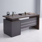 Premium 1.2M Executive Modern Wooden Office Desk in a dark walnut woodgrain finish, featuring a matte charcoal grey front modesty panel with three horizontal silver accent lines, an integrated left-side storage pedestal cabinet, a desktop supporting a modern clock, pen organizer, notebook, mug, and laptop on a polished white tile floor.