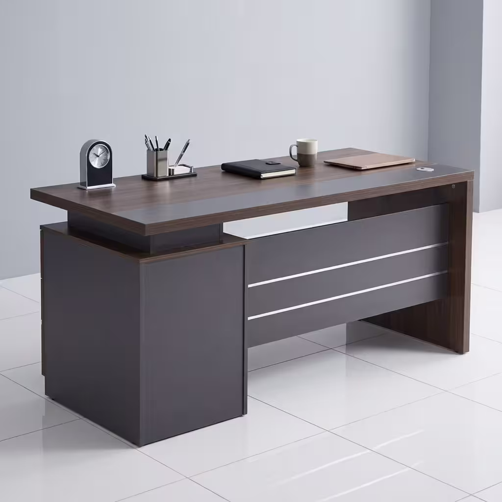 Premium 1.2M Executive Modern Wooden Office Desk in a dark walnut woodgrain finish, featuring a matte charcoal grey front modesty panel with three horizontal silver accent lines, an integrated left-side storage pedestal cabinet, a desktop supporting a modern clock, pen organizer, notebook, mug, and laptop on a polished white tile floor.