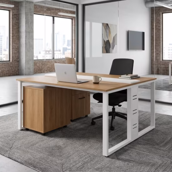 Premium 2-Way Modular Office Workstation featuring two back-to-back light woodgrain desktops, a central white privacy strip, white steel loop base legs, an integrated woodgrain drawer pedestal with a key lock, displaying a keyboard, a laptop, and a desk lamp on a geometric grey carpet.
