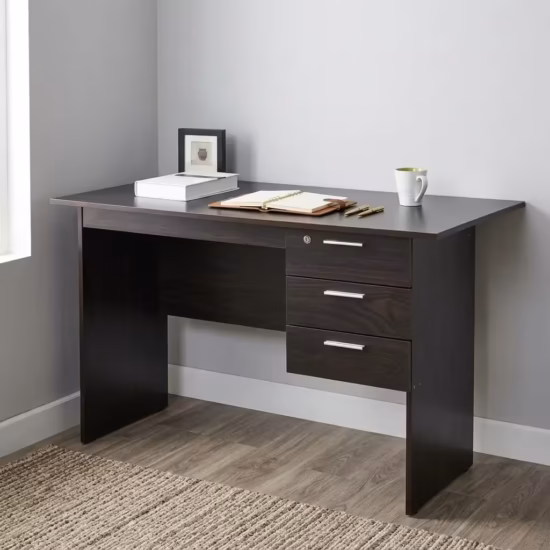 Premium 1.2M Wooden Custom Office/Home Desk in a dark espresso woodgrain finish, showcasing a flat rectangular tabletop supporting an open notebook and book, an integrated 3-drawer storage pedestal with a top key lock and silver bar handles, standing on wood-paneled flooring next to a textured beige rug