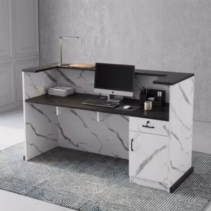 Premium 1.6M Office Front Reception Desk featuring a white marble-patterned panel facade with a center-set black rectangular accent plaque, a thick matte black privacy transaction top supporting a desktop monitor, desk lamp, and a grey ceramic mug, resting on a polished concrete floor against a dark navy wall.