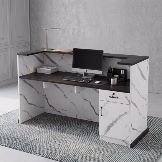 Premium 1.6M Office Front Reception Desk featuring a white marble-patterned panel facade with a center-set black rectangular accent plaque, a thick matte black privacy transaction top supporting a desktop monitor, desk lamp, and a grey ceramic mug, resting on a polished concrete floor against a dark navy wall.