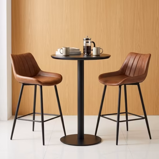 Premium Home Bar Cocktail Table Set featuring a round matte black pedestal table holding a stack of books and a mug, flanked by two matching biscuit-stitched brown faux leather bar stools with black steel frames.