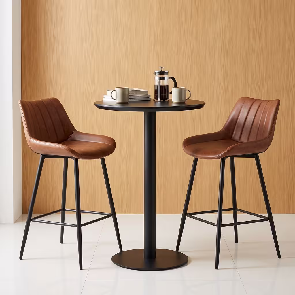 Premium Home Bar Cocktail Table Set featuring a round matte black pedestal table holding a stack of books and a mug, flanked by two matching biscuit-stitched brown faux leather bar stools with black steel frames.