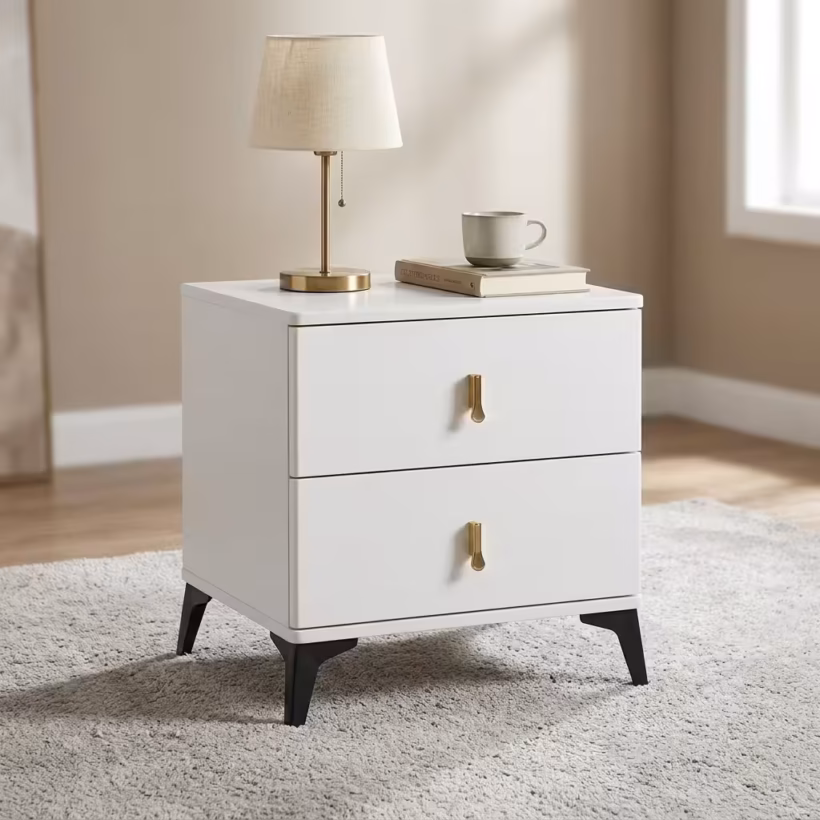 Modern 2-Drawer Bedside Table wrapped in cream microfiber leather with gold-accented metal legs and handles, standing beside a minimalist bed setup.
