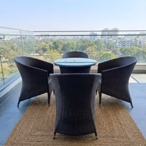 Luxury 4-Seater Rattan Outdoor furniture set featuring four dark hand-woven wicker armchairs and a circular glass-top table on a woven mat on a scenic balcony.