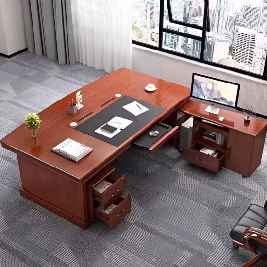 Premium L-Shaped Desk With Side Return in a rich mahogany finish, featuring an integrated black leather center desk blotter mat, a front modesty panel with a diamond-embossed black faux leather center design, and an attached side return console supporting an open laptop, paired with a high-back black mesh office chair on a polished wood floor.