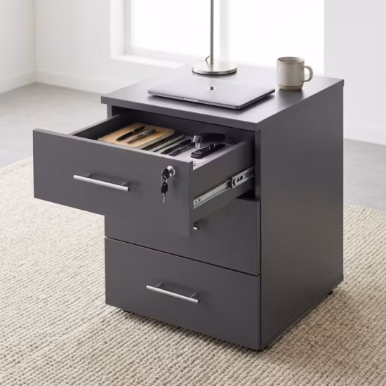 Two premium 3-Drawer Lockable Mobile Pedestals placed side by side on a polished grey concrete floor, showing one finished in a light oak woodgrain and the other in a matte graphite grey, each featuring an open top drawer with a key inserted, revealing a lavender purple inner lining and folder files.