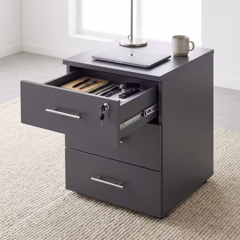 Two premium 3-Drawer Lockable Mobile Pedestals placed side by side on a polished grey concrete floor, showing one finished in a light oak woodgrain and the other in a matte graphite grey, each featuring an open top drawer with a key inserted, revealing a lavender purple inner lining and folder files.