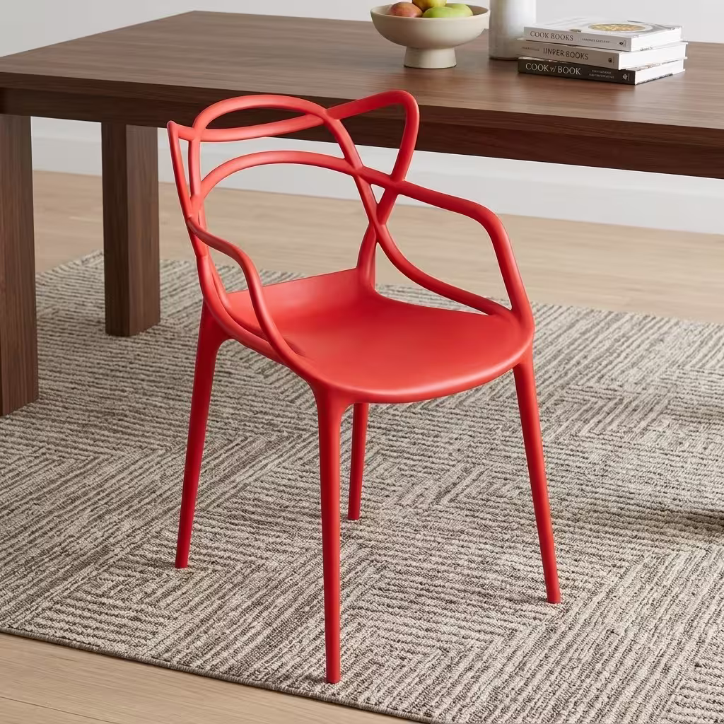 Premium Modern Plastic Outdoor Dining Chair in a vibrant coral-red matte finish, showcasing an intricate interlocking loop open-back silhouette, integrated sweeping armrests, and matching tapered legs, resting on a textured geometric gray area rug next to a walnut wood dining table.