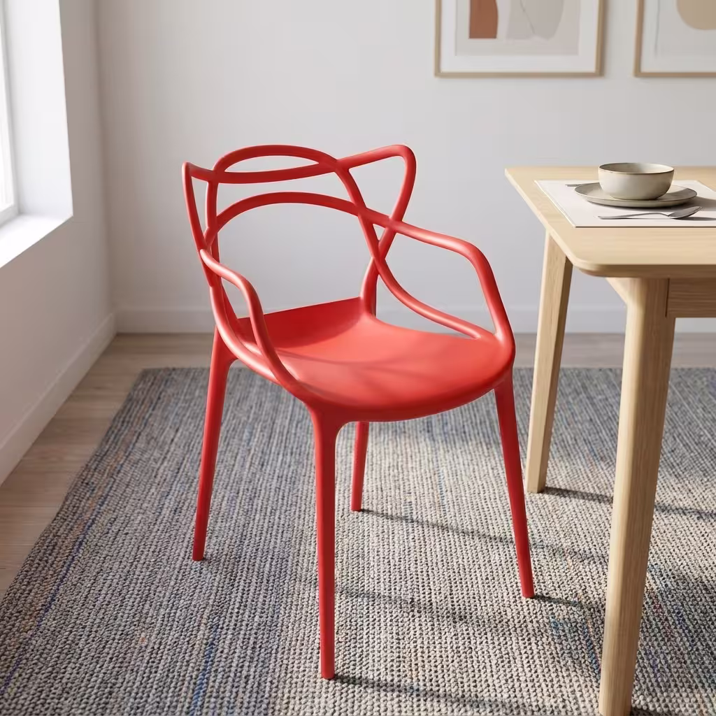 Premium Modern Plastic Outdoor Dining Chair in a vibrant coral-red matte finish, showcasing an intricate interlocking loop open-back silhouette, integrated sweeping armrests, and matching tapered legs, resting on a textured geometric gray area rug next to a walnut wood dining table.