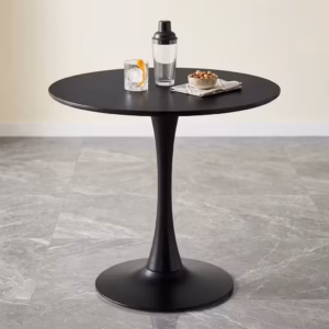 Premium Modern Round Cocktail Table featuring a smooth circular matte black tabletop, supported by a matching matte black trumpet pedestal base, displaying a glass and cocktail shaker on a grey marble tile floor.