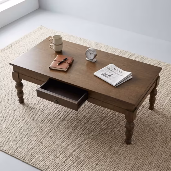 Premium Wooden Coffee Table With Storage in a rich mahogany finish, showcasing a central drawer with a metallic ring pull, a slatted bottom shelf, and carved turned legs on a plush area rug.