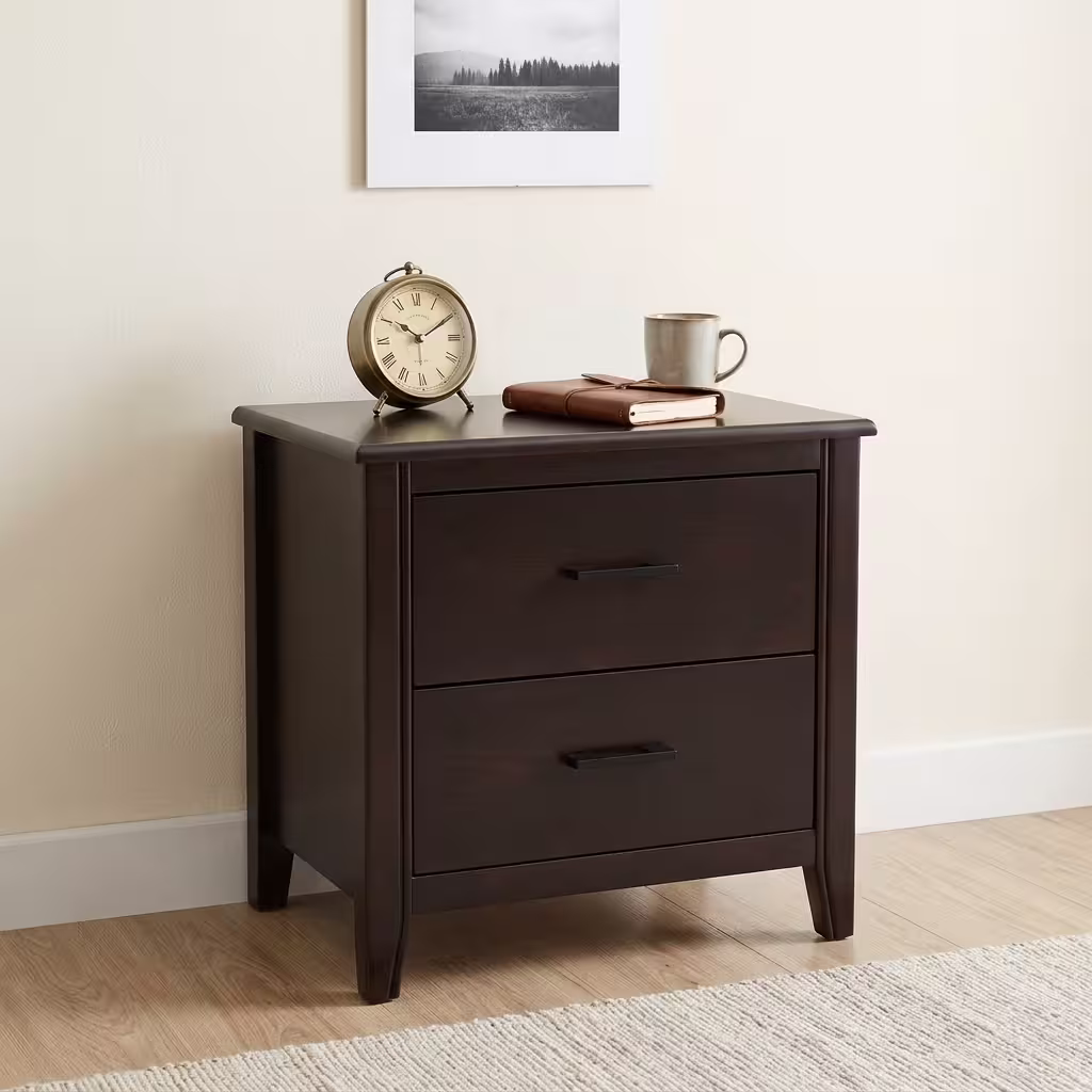 Premium 2-Drawer Modern Bedside Table in a rich espresso finish, showcasing two closed drawers with matte black horizontal pull handles, a tabletop supporting a vintage brass table clock, a leather journal, and a ceramic mug, resting on a textured light cream area rug next to light wood flooring.