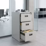 Premium 3-Drawer Cabinet With Single-Key in a professional light gray powder-coated steel finish, showing all three drawers staggered open to reveal legal hanging file tabs, complete with a key inserted in the top lock core, a stapler, and a tape dispenser on top, resting on large gray floor tiles in a glass-partitioned modern office.