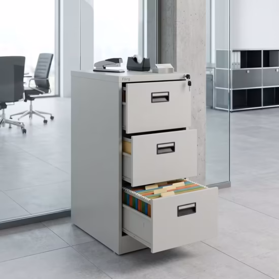 Premium 3-Drawer Cabinet With Single-Key in a professional light gray powder-coated steel finish, showing all three drawers staggered open to reveal legal hanging file tabs, complete with a key inserted in the top lock core, a stapler, and a tape dispenser on top, resting on large gray floor tiles in a glass-partitioned modern office.