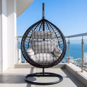 Premium 1-Seater Modern Rattan Hammock Swing featuring a black hand-woven teardrop wicker basket, a heavy-duty dark gray steel hanging stand, and plush black-and-white plaid cushions, placed on a high-rise balcony overlooking a city skyline.