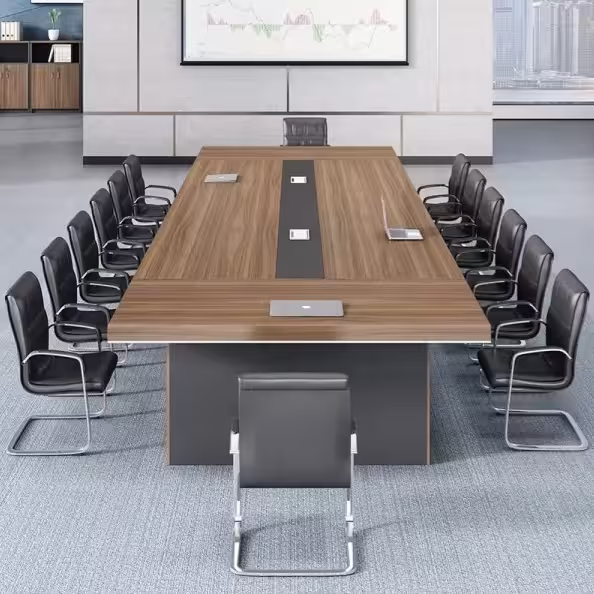 Premium 14-16 Seater Modern Conference Table in a rich walnut woodgrain finish, showcasing a massive rectangular top panel with a center-running black accent band and four silver flip-top power grommets supporting an open laptop, anchored by three heavy-duty matte charcoal gray block leg pillars, resting on a textured blue area rug in a modern office setup with matching wood storage cabinets in the background.
