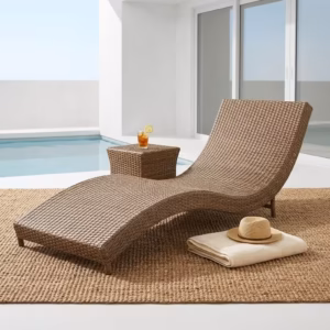 Premium Outdoor Rattan Sun Lounger featuring an ergonomically curved hand-woven natural-tone wicker frame, a plush off-white water-resistant full-length cushion, styled with two blue accent pillows, resting on a textured woven jute rug near a small wooden side table.