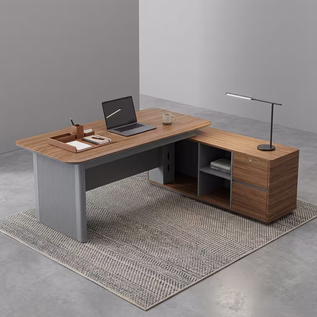 Premium 1600MM Executive L-Shaped Office Desk featuring a rich walnut woodgrain finish, a matte grey vertical fluted slatted front modesty panel, and an attached side return storage console supporting a tablet stand, laptop, coffee mug, and notebooks, paired with a high-back black mesh office chair on a textured cream area rug.