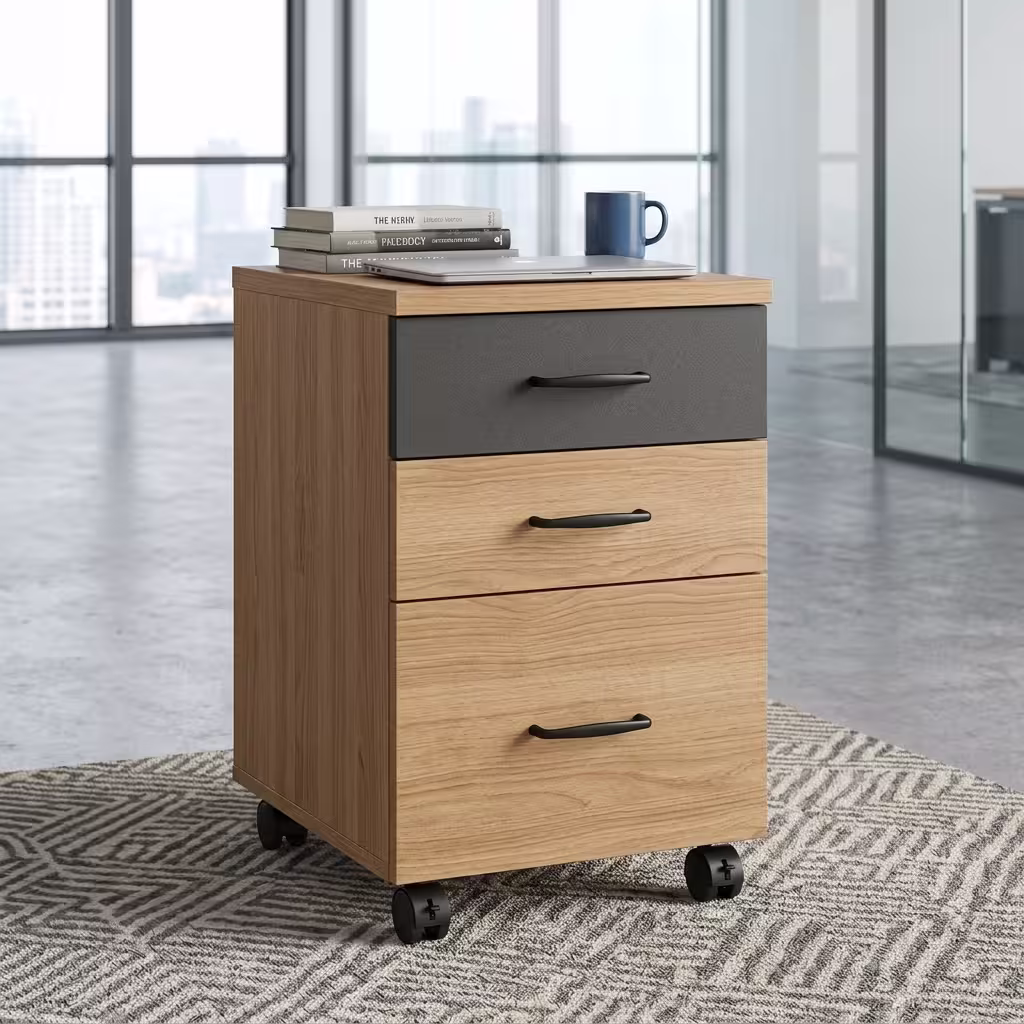 3-Drawer Modern Wooden Mobile Pedestal Premium 3-Drawer Modern Wooden Mobile Pedestal featuring a natural light oak woodgrain finish, an upper storage drawer in contrasting matte charcoal grey, two lower light oak drawers, all equipped with curved matte black handles, supporting a mug, stapler, and notebooks on top, resting on a textured geometric carpet.