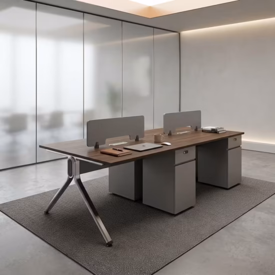Premium 4-Way Modern Staff Office Workstation featuring a 4-person back-to-back island layout with walnut woodgrain desktops, integrated matte grey privacy partition screens, a heavy-duty angled aluminum A-frame base, and a central box wire enclosure, paired with four black mesh visitor chairs with chrome cantilever sled bases, resting on a textured beige area rug inside a modern minimalist office.