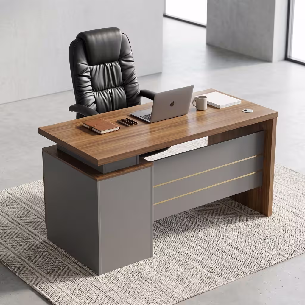 Executive 1.4M Office Desk With Drawers Premium Executive 1.4M Office Desk With Drawers featuring a rich walnut woodgrain top panel, supported by a front modesty shield in a matte grey finish decorated with three horizontal gold accent lines, an integrated left-side return storage console block, a desktop supporting an open silver laptop, a leather notebook with three pens, a ceramic mug, and a closed white book, paired with a high-back black leather executive chair, resting on a textured chevron-patterned woven area rug over a polished concrete floor.
