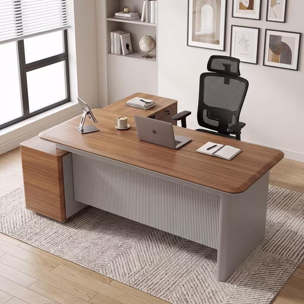 Premium 1600MM Executive L-Shaped Office Desk featuring a rich walnut woodgrain finish, a matte grey vertical fluted slatted front modesty panel, and an attached side return storage console supporting a tablet stand, laptop, coffee mug, and notebooks, paired with a high-back black mesh office chair on a textured cream area rug.