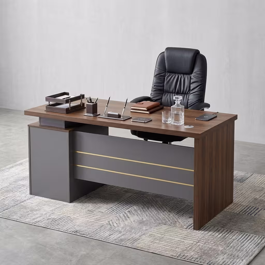 Premium Executive 1.4M Office Desk With Drawers featuring a rich walnut woodgrain top panel, supported by a front modesty shield in a matte grey finish decorated with three horizontal gold accent lines, an integrated left-side return storage console block, a desktop supporting an open silver laptop, a leather notebook with three pens, a ceramic mug, and a closed white book, paired with a high-back black leather executive chair, resting on a textured chevron-patterned woven area rug over a polished concrete floor.