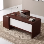 Premium 1.8M Custom Office Desk With Mobile Extension in a deep cherry-mahogany woodgrain finish, featuring an off-white front modesty panel, an integrated left-side storage console, an attached side return cabinet supporting an open laptop computer on a dark brown leather desk blotter mat, a classic silver articulating arm desk lamp, and stacked books, resting on an ornate patterned traditional area rug.