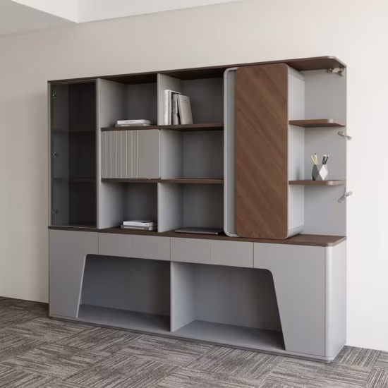Premium Executive Modern Office Wooden Cabinet in a dual-tone matte grey and walnut woodgrain finish, showcasing a tinted smoked-glass case on the left, open book shelves with a grey ribbed sliding door, a vertical rounded wood panel block on the right next to open side shelving with a pen holder, and lower push-open drawers above a geometric open base cutout, standing on grey textured office carpet tiles.