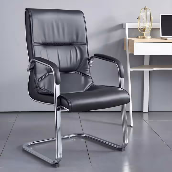 Premium PU Leather Office Visitor Chair featuring a black leatherette mid-backrest with horizontal pleat lines, integrated chrome armrests with matching black top pads, and a highly reflective continuous chrome steel cantilever sled frame, standing on large grey tile flooring next to a small wooden desk.
