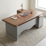 Premium 2.0M Executive L-Shaped Office Desk featuring a rich walnut woodgrain finish, an integrated tan leather desk blotter mat supporting an open laptop computer and a wireless mouse, a front modesty panel with a wave-curved matte grey design, and an attached side return storage console supporting a minimalist table lamp, resting on a textured cream and brown area rug.