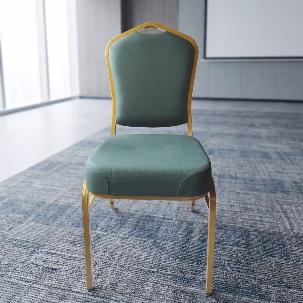 Premium Heavy Duty Green Banquet Seat featuring a crown-arched backrest and thick box seat cushion upholstered in plush teal velvet, supported by an industrial-strength metallic gold-finished steel frame, standing on a dark grey patterned carpet inside a modern seminar hall.