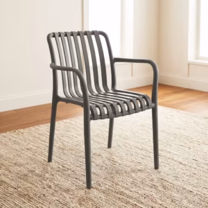 Premium Stackable Plastic Bistro Chair in a deep matte navy blue finish, showcasing a single-piece molded resin frame with an open vertical slatted backrest and seat, sweeping integrated armrests, and clean tapered legs, standing on a textured sisal area rug in a sunlit interior room by a window.