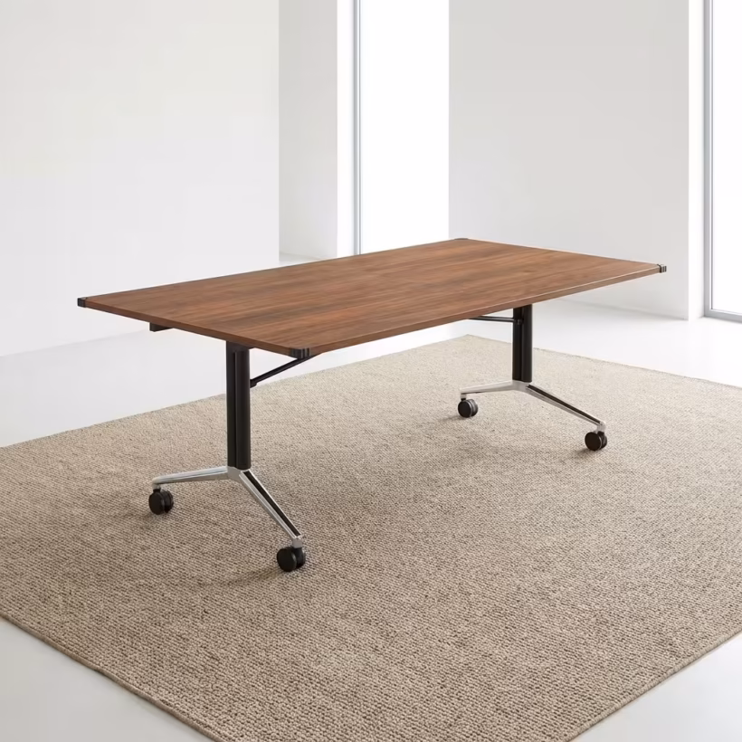 Premium Mobile Foldable Office Boardroom Table in a rich walnut woodgrain finish, showcasing a spacious rectangular top panel with protective black plastic corner guards, supported by an industrial steel T-bar frame base featuring matte black columns and highly reflective polished chrome feet fitted with four black locking twin-wheel casters, resting on a textured beige area rug.