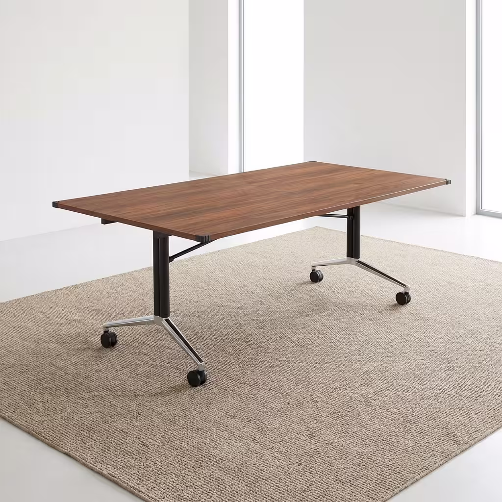 Premium Mobile Foldable Office Boardroom Table in a rich walnut woodgrain finish, showcasing a spacious rectangular top panel with protective black plastic corner guards, supported by an industrial steel T-bar frame base featuring matte black columns and highly reflective polished chrome feet fitted with four black locking twin-wheel casters, resting on a textured beige area rug.