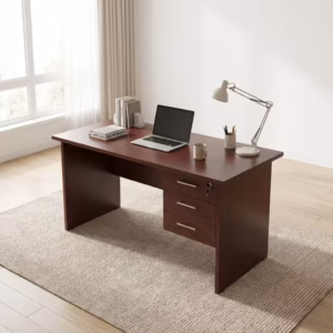 Premium 1M Wooden Lockable Study Desk in a mahogany woodgrain finish, showcasing a spacious rectangular top panel holding an open laptop, a ceramic mug, and books, an integrated three-drawer right storage pedestal with silver handles and a key inserted in the top lock core, a white articulation desk lamp, resting on a textured cream area rug over light wood flooring.