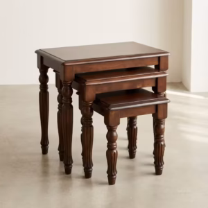 Premium Classic Wooden Nesting Stool Set in a rich dark walnut woodgrain finish, showcasing three stacked rectangular accent tables with ornate hand-carved column legs graduated by size, standing flat on smooth light grey flooring inside a bright contemporary minimalist room.