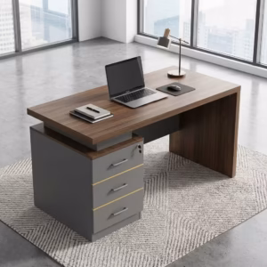 Premium 120cm Executive Desk With Lockable Drawers featuring a rich walnut woodgrain top panel, an integrated matte charcoal gray 3-drawer storage pedestal on the left with silver handles and gold trim, an open laptop, mouse pad, and notebooks on top, resting on a textured geometric cream area rug over a polished concrete floor.