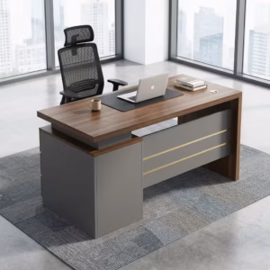 Premium 120cm Executive Desk With Lockable Drawers featuring a rich walnut woodgrain top panel, an integrated matte charcoal gray 3-drawer storage pedestal on the left with silver handles and gold trim, an open laptop, mouse pad, and notebooks on top, resting on a textured geometric cream area rug over a polished concrete floor.