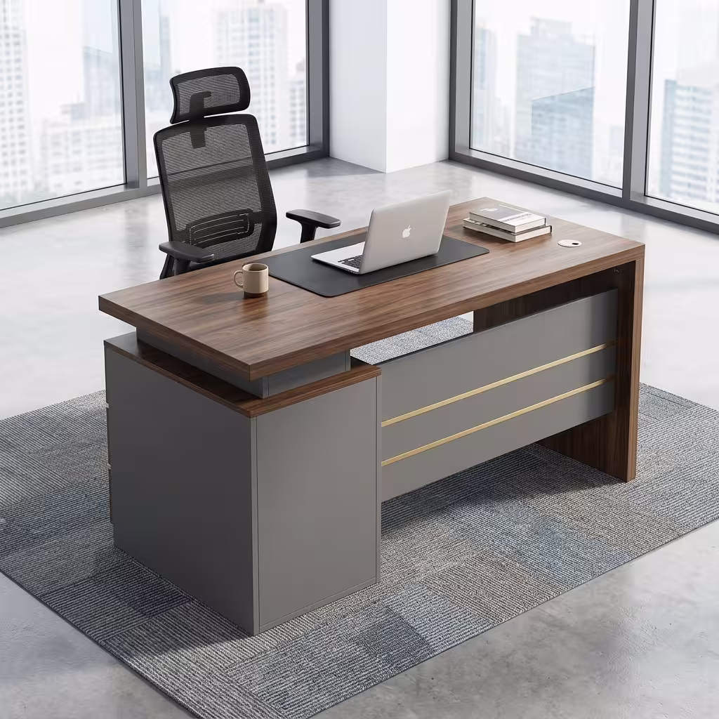 Premium 120cm Executive Desk With Lockable Drawers featuring a rich walnut woodgrain top panel, an integrated matte charcoal gray 3-drawer storage pedestal on the left with silver handles and gold trim, an open laptop, mouse pad, and notebooks on top, resting on a textured geometric cream area rug over a polished concrete floor.
