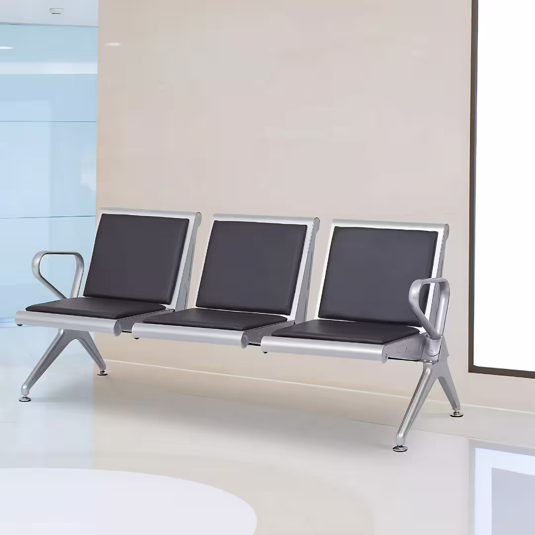 Premium 3-Seater Padded Metallic Waiting Bench featuring three linked silver metallic chairs with black padded leatherette seats and backrests, integrated curved aluminum-alloy side armrests, and sturdy silver metal triangle legs with adjustable leveling glides, standing on a reflective white floor inside a modern corporate reception room.