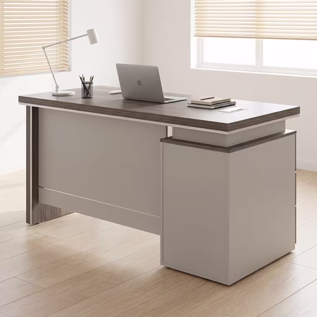 Premium 1200mm Grey Oak Executive Office Desk featuring a rich dark grey oak woodgrain top panel, supported by a front modesty shield in a matte grey finish, an integrated side return storage console block, a desktop supporting an open silver laptop, a white ceramic pen cup, a white desk lamp, and closed journals, resting on a textured woven area rug over light flooring.