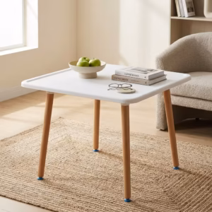 Premium 4-Seater Square Wooden Dining Table in an elegant matte white and natural wood dual-tone finish, showcasing a square tray-style top panel holding a ceramic coffee mug, a leather notebook with a pen, and a closed white hardbound book, supported by four tapered round solid beechwood legs, resting on a textured geometric cream area rug over polished tile flooring.